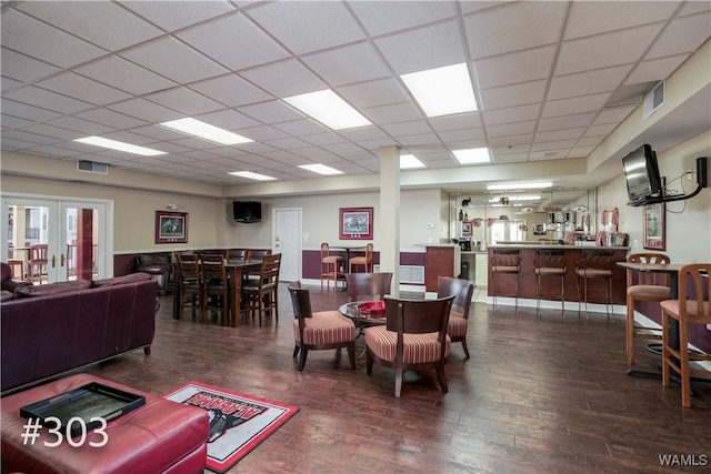 living room with a drop ceiling, dark hardwood / wood-style floors, french doors, and indoor bar