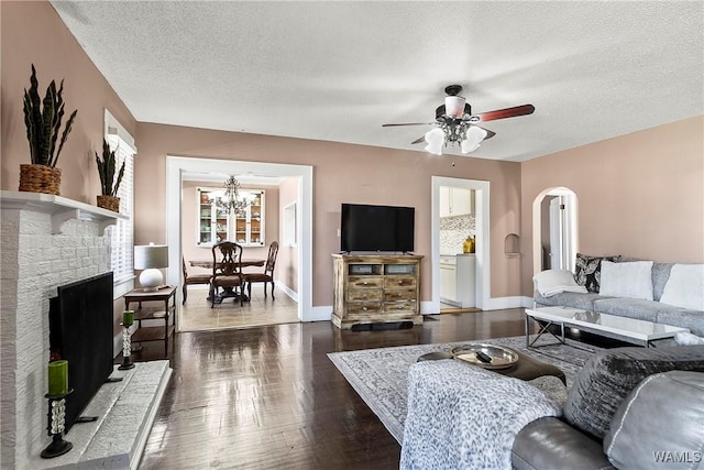 living room featuring ceiling fan with notable chandelier, a fireplace, dark hardwood / wood-style floors, and a textured ceiling