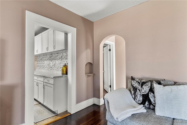 interior space featuring arched walkways, dark wood finished floors, backsplash, a textured ceiling, and baseboards