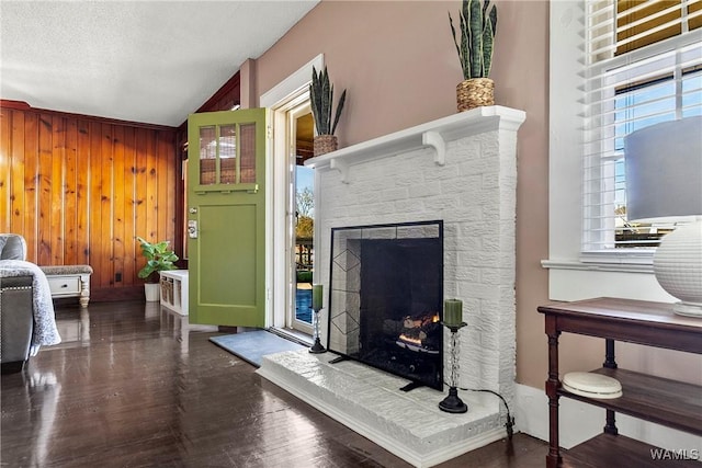 living room featuring dark wood-type flooring, a fireplace, a textured ceiling, vaulted ceiling, and wood walls