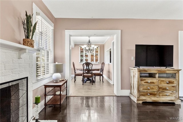 living room with baseboards, a chandelier, wood finished floors, and a stone fireplace