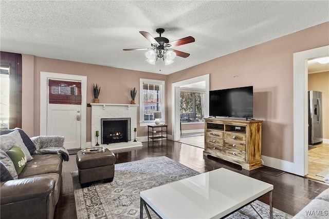 living room featuring a textured ceiling, a fireplace, wood finished floors, a ceiling fan, and baseboards