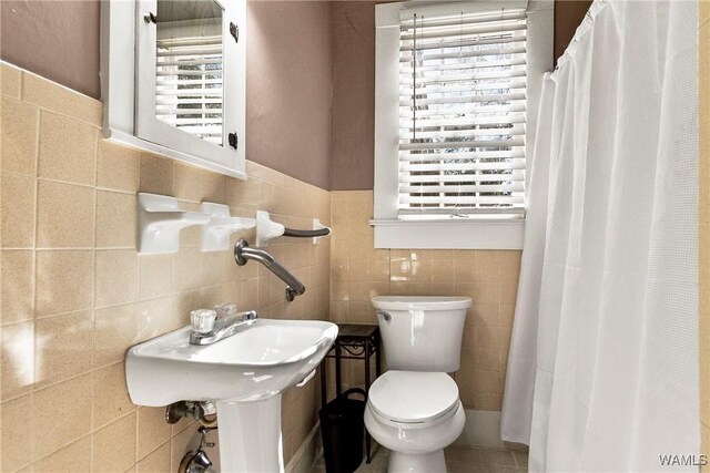 bathroom featuring a wainscoted wall, a shower with shower curtain, toilet, and tile walls