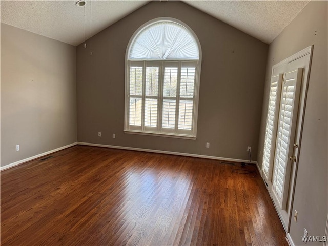 spare room featuring a textured ceiling, dark hardwood / wood-style floors, and vaulted ceiling