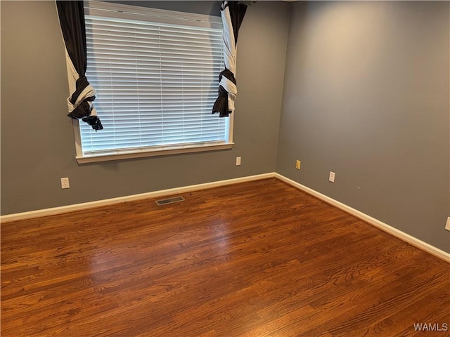 unfurnished room featuring baseboards, visible vents, and wood finished floors