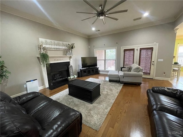 living area featuring a fireplace with flush hearth, wood finished floors, visible vents, baseboards, and ornamental molding