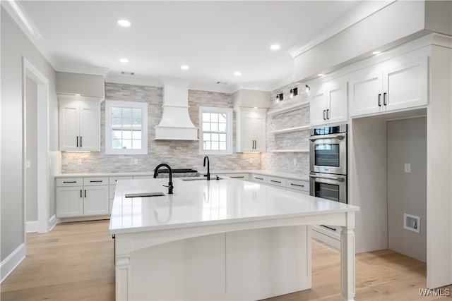 kitchen with custom range hood, stainless steel appliances, sink, a center island with sink, and white cabinets