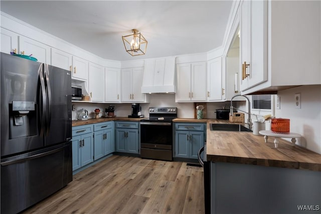 kitchen with a sink, butcher block counters, stainless steel appliances, custom range hood, and blue cabinets
