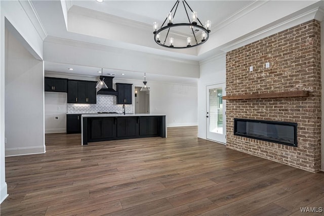 kitchen with ornamental molding, custom range hood, a raised ceiling, and a center island with sink