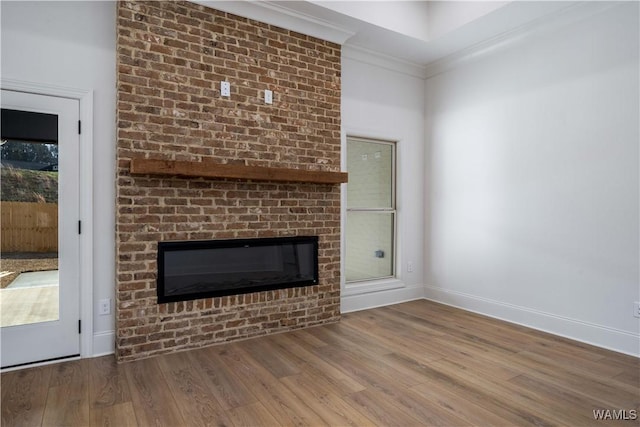 unfurnished living room featuring a brick fireplace, wood-type flooring, and ornamental molding