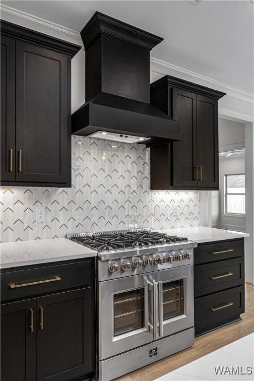 kitchen featuring high end stove, ornamental molding, custom range hood, light hardwood / wood-style floors, and decorative backsplash