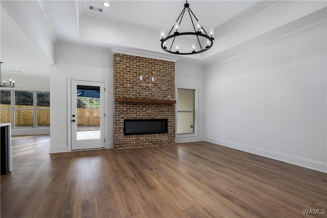 unfurnished living room with wood-type flooring, a notable chandelier, a raised ceiling, crown molding, and a brick fireplace