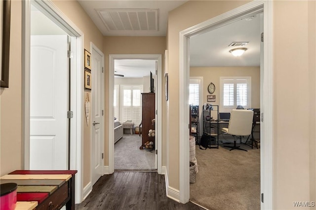 hall with visible vents, dark carpet, and baseboards