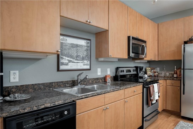 kitchen with light wood-type flooring, a sink, dark stone counters, and appliances with stainless steel finishes