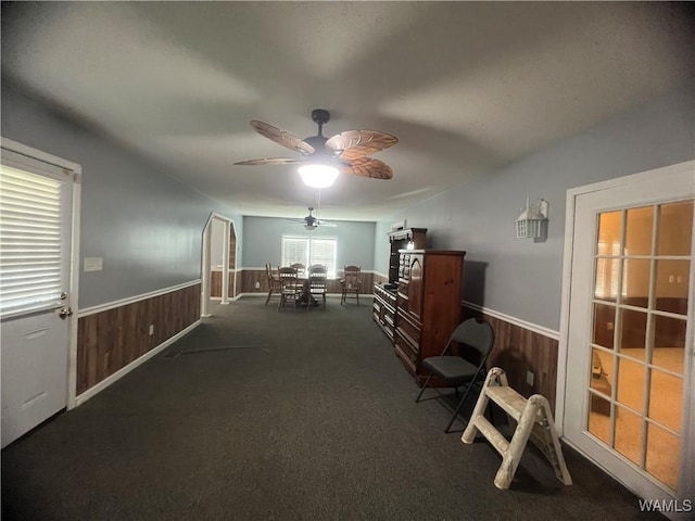 interior space with a wainscoted wall, wooden walls, and ceiling fan