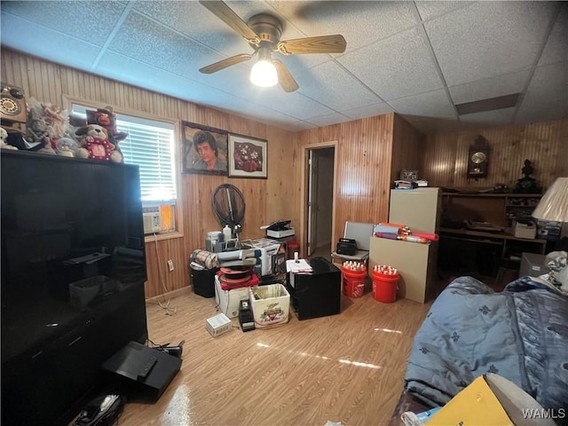 bedroom with ceiling fan, wood finished floors, a drop ceiling, and wood walls