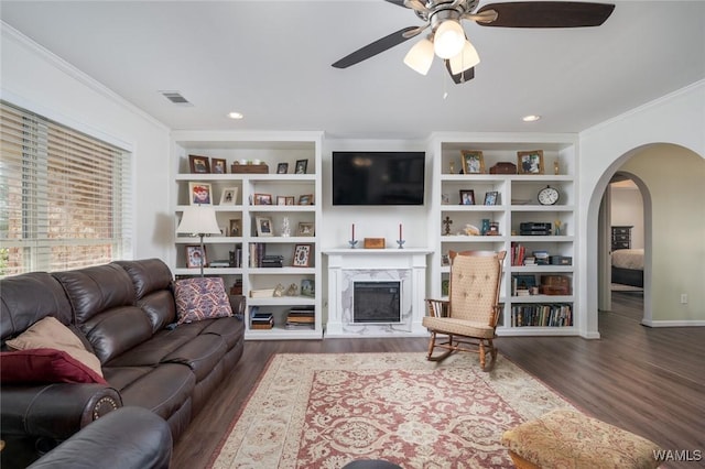 living area featuring a high end fireplace, arched walkways, dark wood-style flooring, and ornamental molding