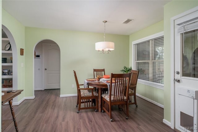 dining area featuring arched walkways, visible vents, baseboards, dark wood-style floors, and an inviting chandelier