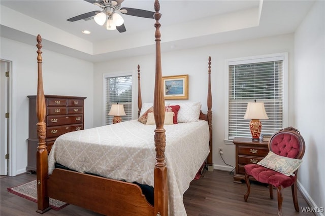 bedroom with dark wood-type flooring, a raised ceiling, and baseboards