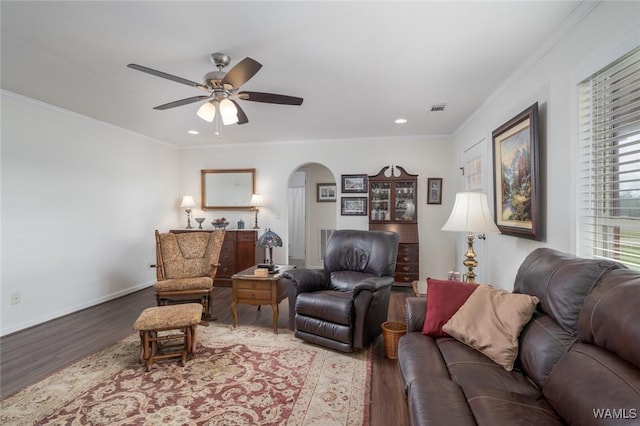 living area featuring arched walkways, crown molding, baseboards, and wood finished floors