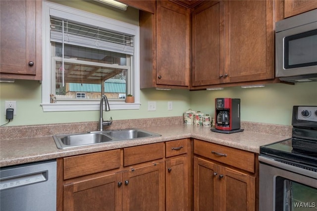 kitchen with brown cabinets, stainless steel appliances, a sink, and light countertops