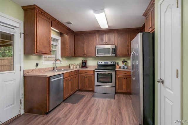 kitchen featuring dark wood finished floors, brown cabinets, stainless steel appliances, light countertops, and a sink