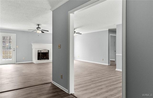 unfurnished living room with a fireplace with raised hearth, a ceiling fan, a textured ceiling, wood finished floors, and baseboards