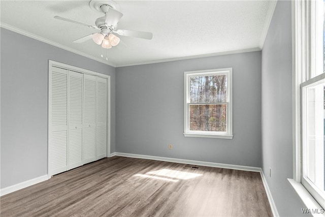 unfurnished bedroom with crown molding, a closet, light wood-style flooring, ceiling fan, and baseboards