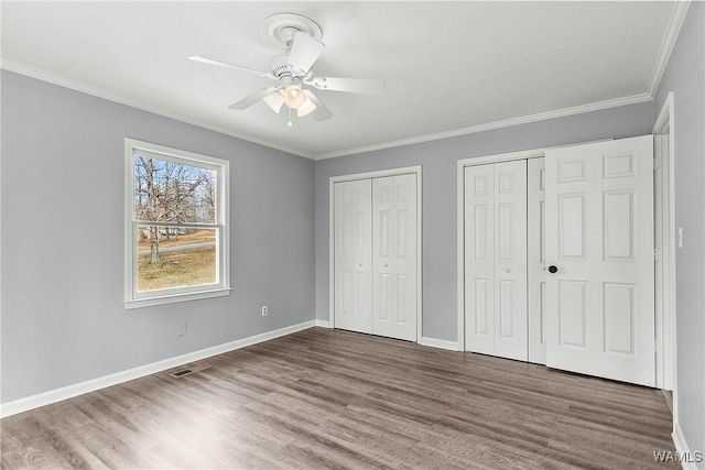 unfurnished bedroom with baseboards, dark wood finished floors, a ceiling fan, crown molding, and two closets