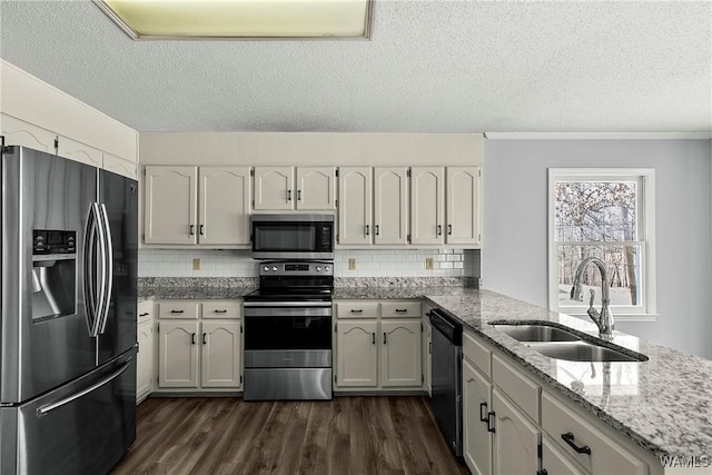 kitchen with light stone counters, stainless steel appliances, a peninsula, a sink, and dark wood finished floors