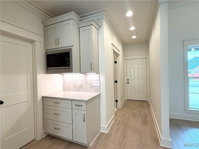 kitchen with built in microwave, backsplash, light wood-style floors, crown molding, and light countertops