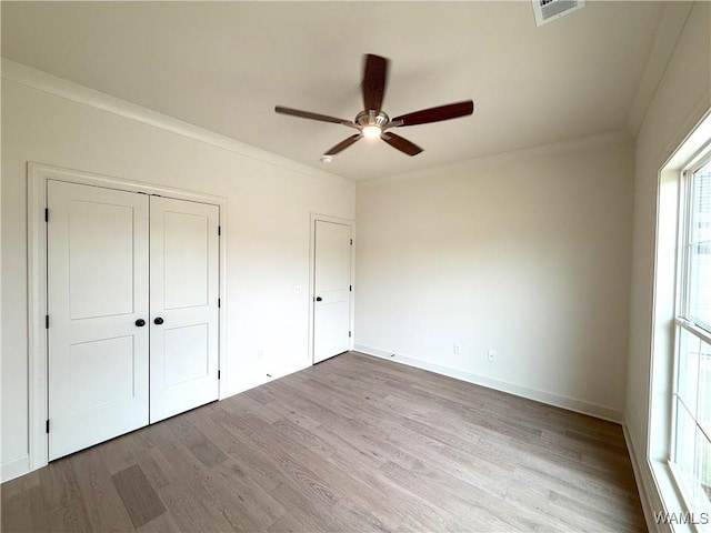 unfurnished bedroom featuring wood finished floors, a closet, ceiling fan, baseboards, and visible vents