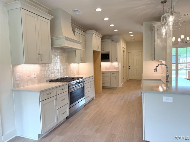 kitchen featuring a sink, stainless steel gas range, premium range hood, visible vents, and recessed lighting