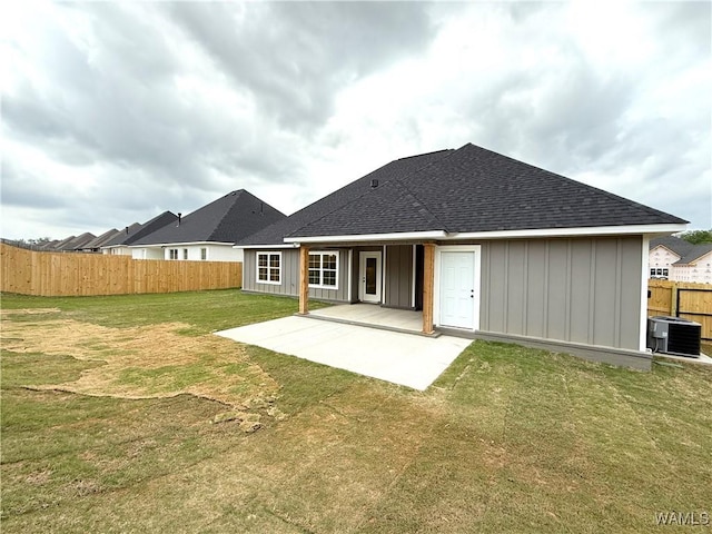 rear view of house featuring fence, a shingled roof, a yard, board and batten siding, and a patio area