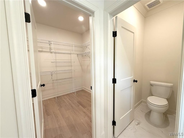 bathroom with a spacious closet, toilet, visible vents, and baseboards