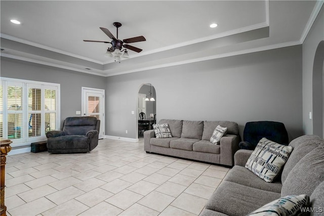 living room with arched walkways, a raised ceiling, a ceiling fan, ornamental molding, and light tile patterned floors