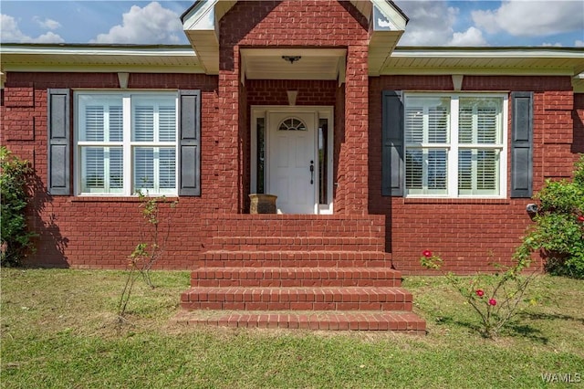 property entrance with a lawn and brick siding