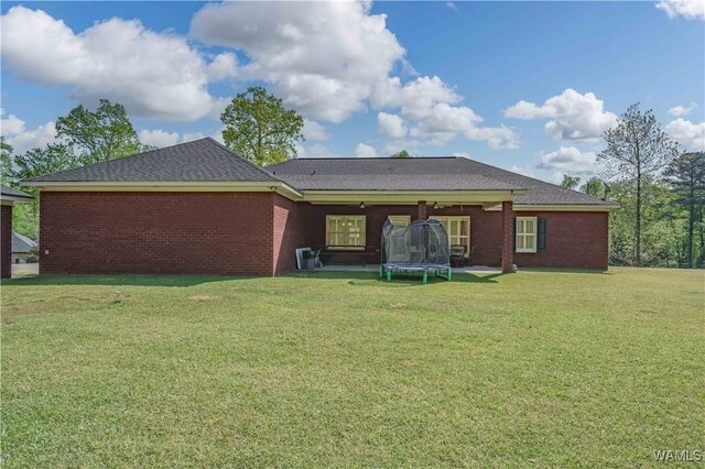 rear view of house with brick siding, a yard, and a trampoline