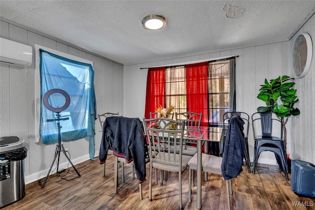 dining space featuring a textured ceiling, a wall unit AC, wood finished floors, and baseboards