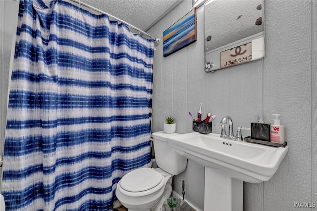 bathroom with a textured wall, toilet, curtained shower, a textured ceiling, and a sink