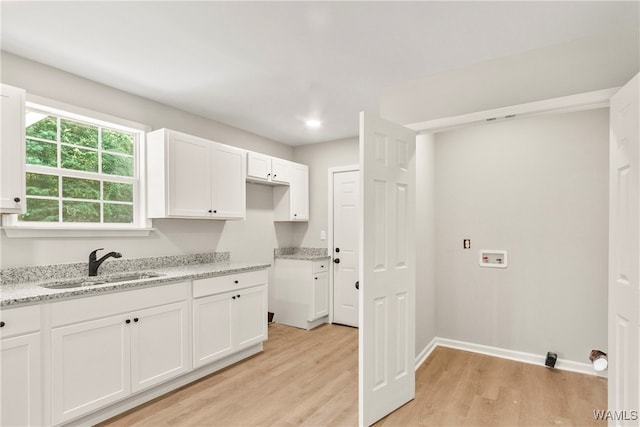 kitchen featuring white cabinetry, light hardwood / wood-style flooring, light stone countertops, and sink