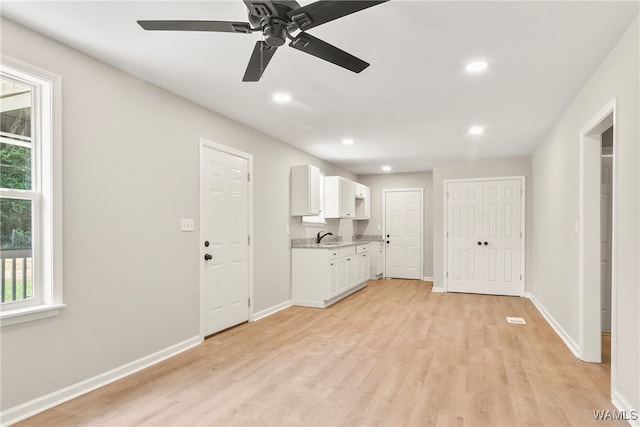 interior space with white cabinets, sink, ceiling fan, light wood-type flooring, and light stone counters