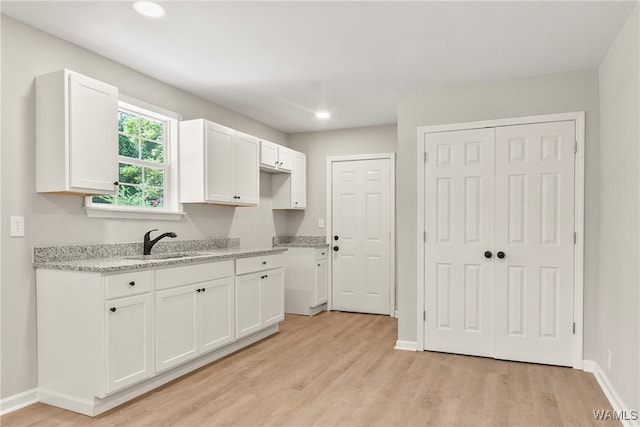 kitchen with white cabinets, light wood-type flooring, light stone countertops, and sink