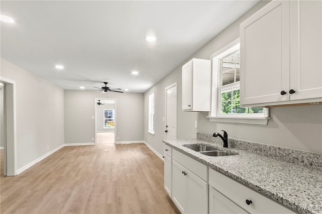 kitchen featuring light stone countertops, light wood-type flooring, white cabinetry, and sink