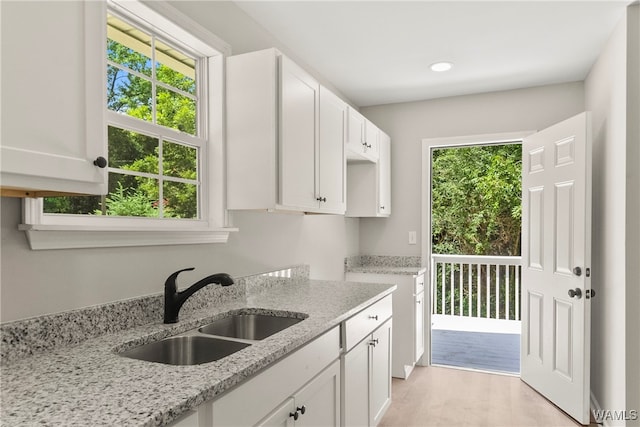 kitchen with white cabinets, light stone counters, and sink