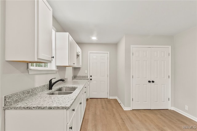 kitchen with light stone counters, light hardwood / wood-style flooring, white cabinetry, and sink