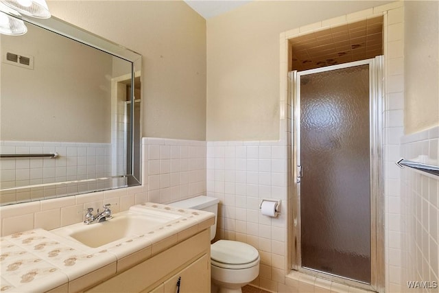 bathroom featuring visible vents, toilet, vanity, a stall shower, and tile walls