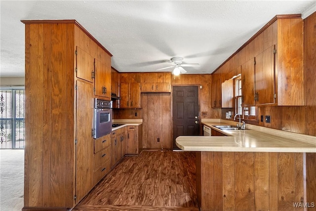 kitchen featuring oven, a textured ceiling, a peninsula, brown cabinetry, and light countertops