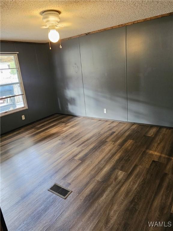 empty room with ceiling fan, a textured ceiling, and dark wood-type flooring