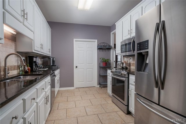 kitchen with appliances with stainless steel finishes, sink, light tile patterned floors, dark stone countertops, and white cabinetry